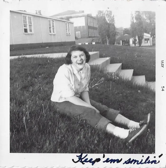 Black and white photo of a smiling woman seated on a lawn noted with Keep Em Smilin and May 1954